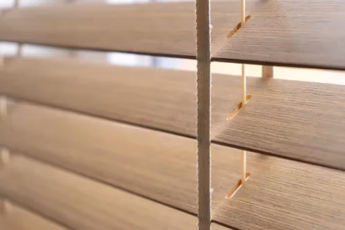 Close-up van beige horizontale raamjaloezieën met zichtbare lamellen en koorden, zacht verlicht door natuurlijk licht dat door het raam valt.
