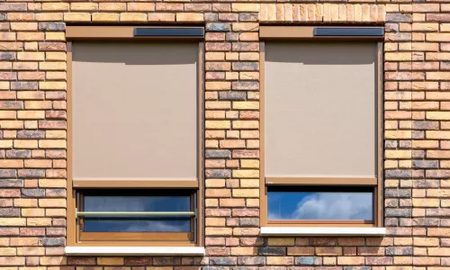 Twee beige ritsscreens met Brel-solarmotor voor ramen in een bakstenen gevel